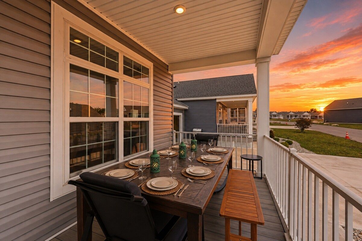 An outdoor dining area with a table set for four, a covered porch, and a view of the sunset.