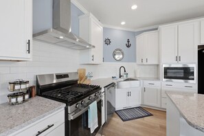 Une cuisine moderne avec des meubles blancs, une hotte en acier inoxydable, un four encastré, un four à micro-ondes et un plan de travail en granit.