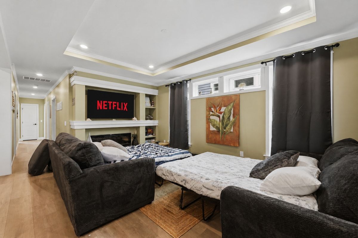 A living room with a sofa, a bed, a fireplace, a TV mounted on the wall, and a painting on the wall.