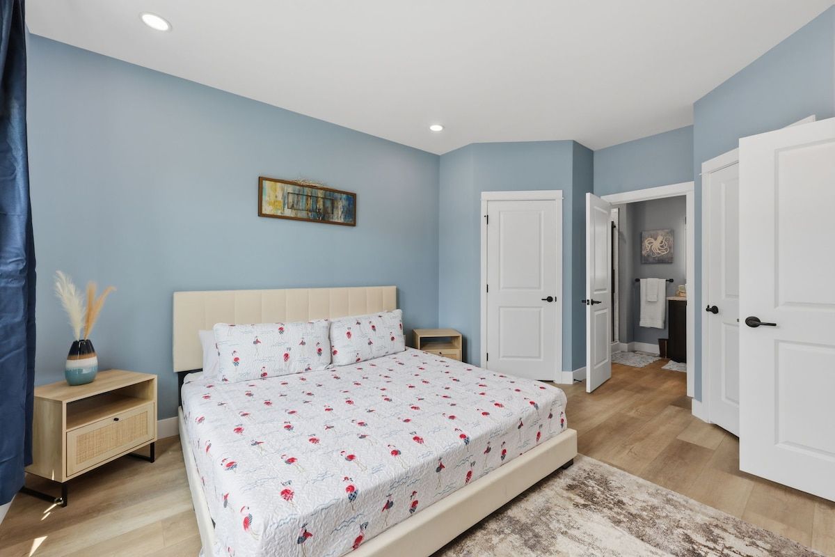 A bedroom with a bed, a nightstand, a dresser, and a door leading to another room.