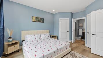 A bedroom with a bed, a nightstand, a dresser, and a door leading to another room.