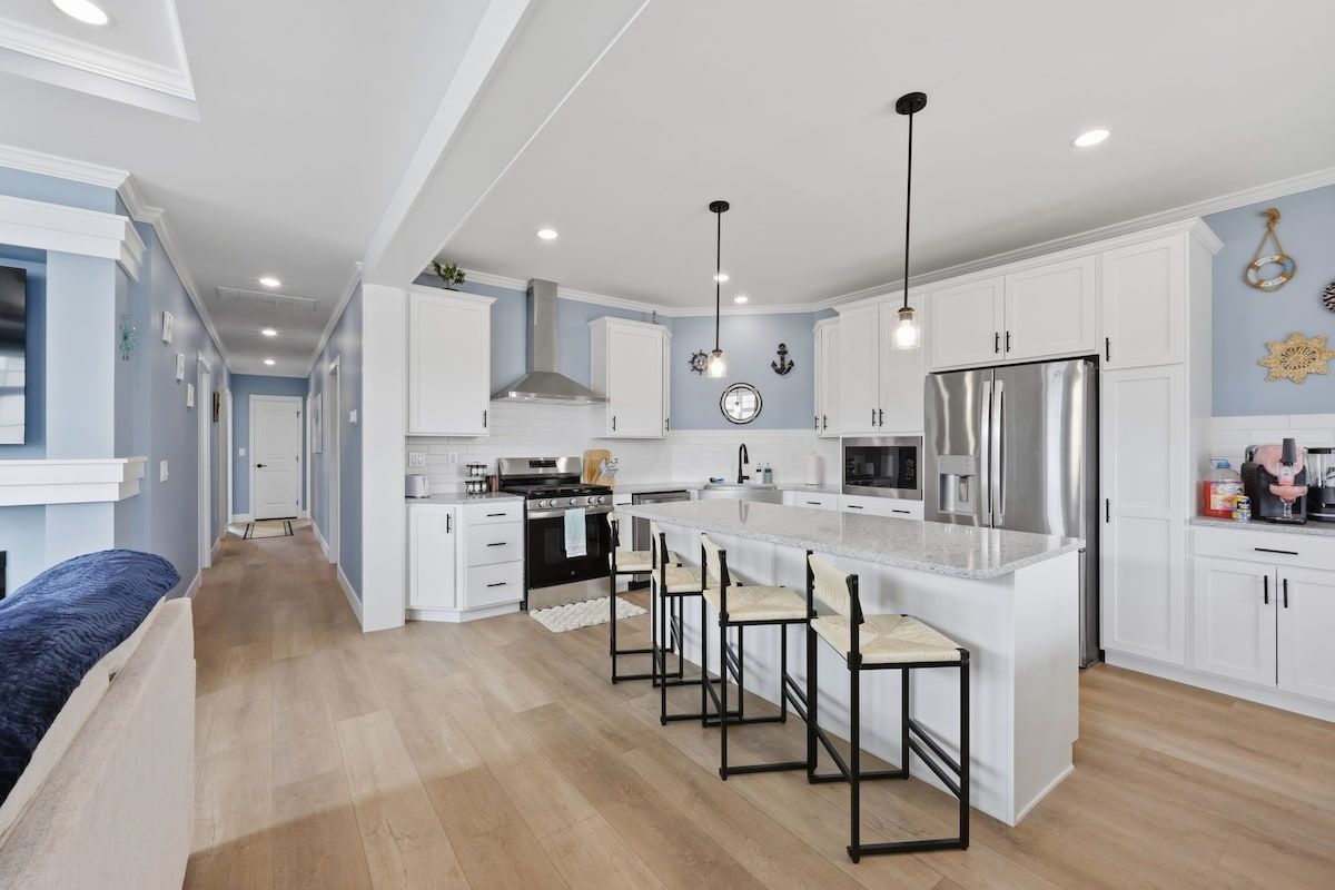 A modern kitchen with white cabinetry, a central island with bar stools, a stainless steel refrigerator, and pendant lighting.