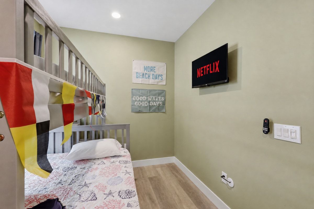 A bedroom with a bed, a TV mounted on the wall, and a sign that says 'NETFLIX'.
