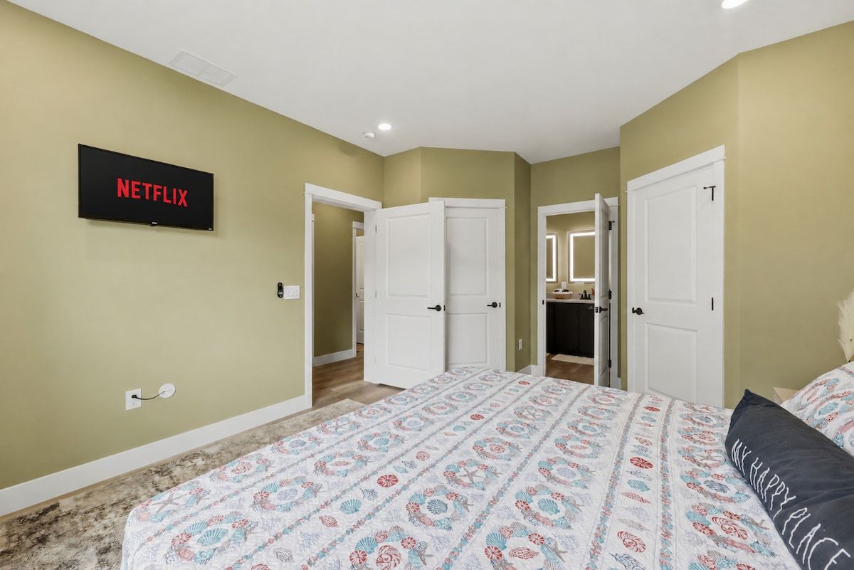 A bedroom with a bed, a wall-mounted TV, and a door leading to a bathroom.