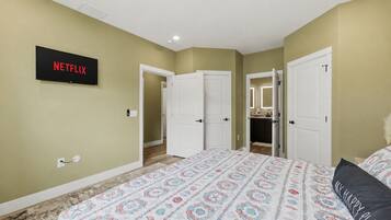 A bedroom with a bed, a wall-mounted TV, and a door leading to a bathroom.
