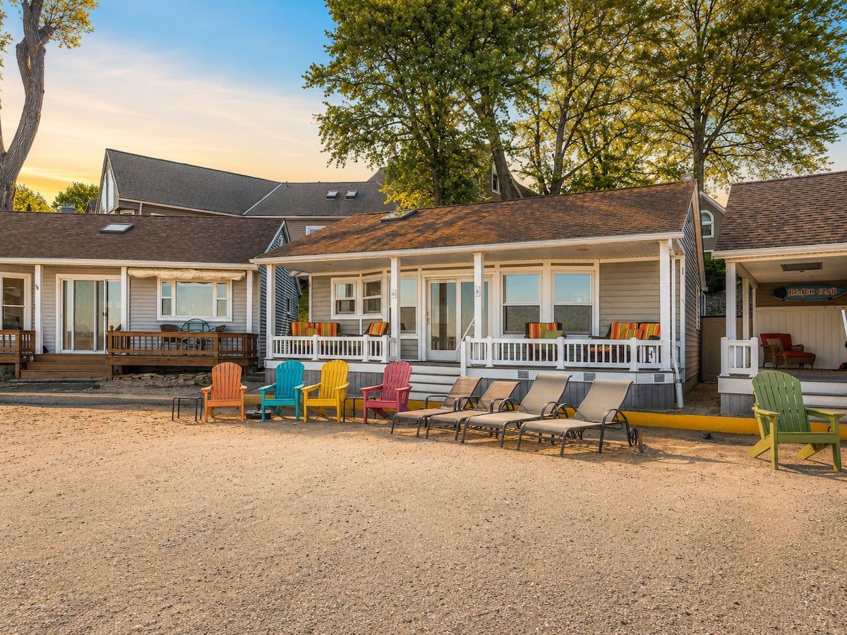 Eine Reihe Strandhäuser mit Kiesterrasse und bunten Adirondack-Stühlen.