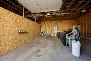 An indoor space with a concrete floor, wooden walls, and a metal ceiling. There are plastic chairs, a white trash bin, and a ladder leaning against the wall. - Lakeside Legend-Hot tub/Pool/Water Views/Billiards (Lakeside Marblehead)
