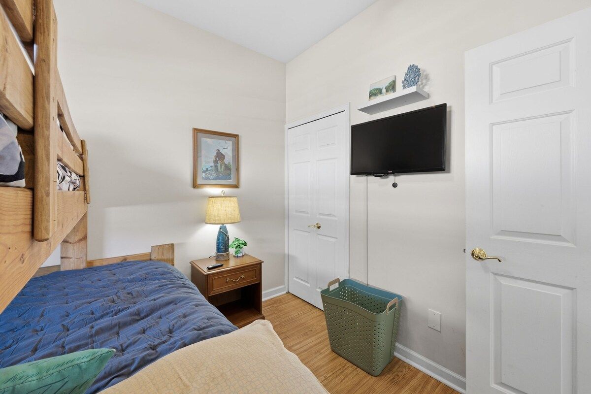 A bedroom with a bed, nightstand, lamp, TV, wardrobe, and a basket.