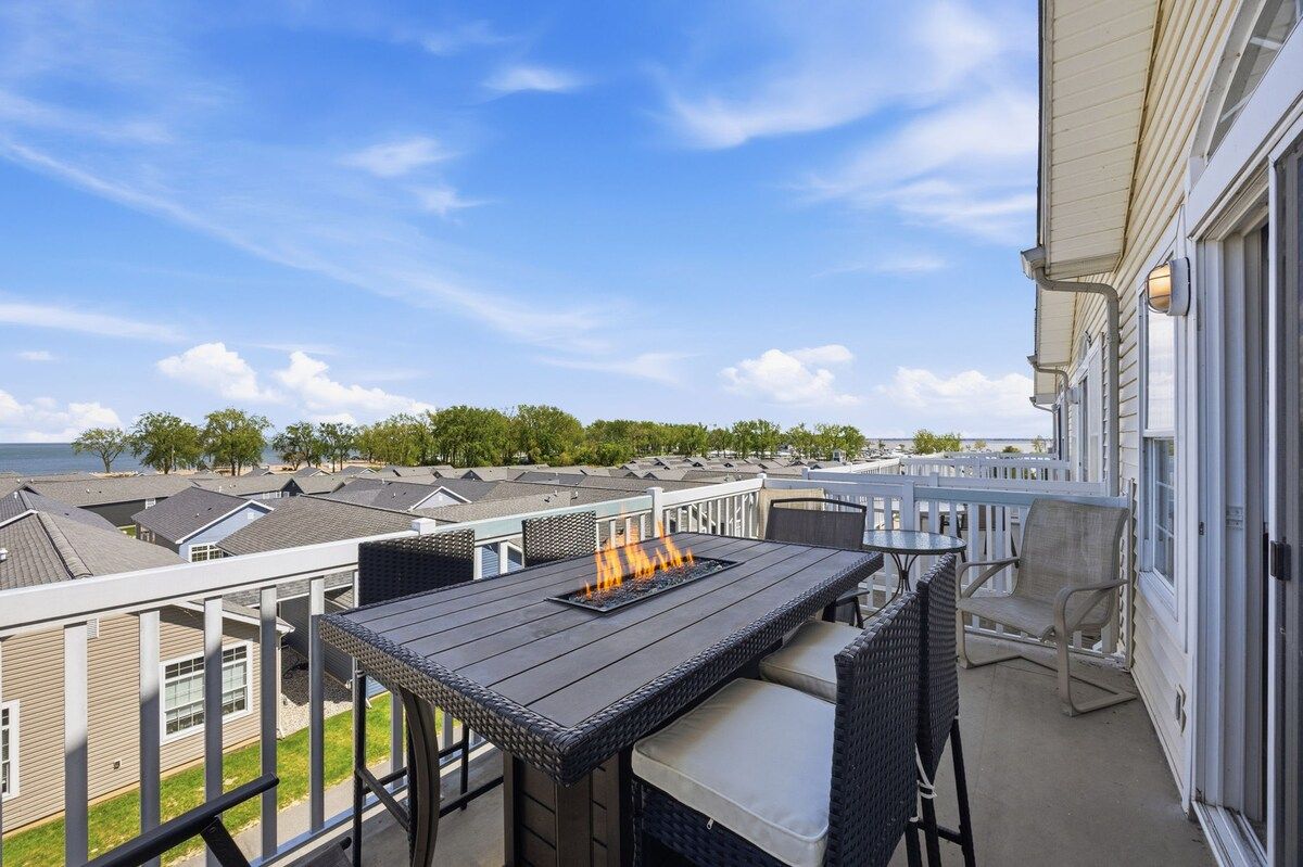 A balcony with a table and chairs, overlooking a row of houses and a body of water.