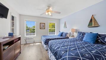 A bedroom with two beds, a ceiling fan, a TV, and a window with a view of greenery.