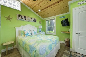 Une chambre avec un lit, une table de chevet, une lampe, une décoration en forme d’étoile de mer, un panneau mural, une fenêtre et une porte portant l’inscription « PLAGE ».