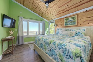 Quarto com cama, televisão, janela com cortinas e ventilador de teto.