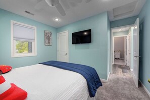 Een slaapkamer met een bed, een plafondventilator, een televisie en een deur naar een andere kamer.
