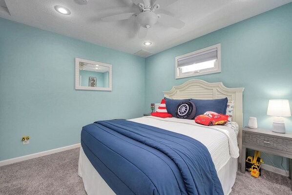 Ein Schlafzimmer mit einem Bett, Deckenventilator, Nachttisch und Lampe.