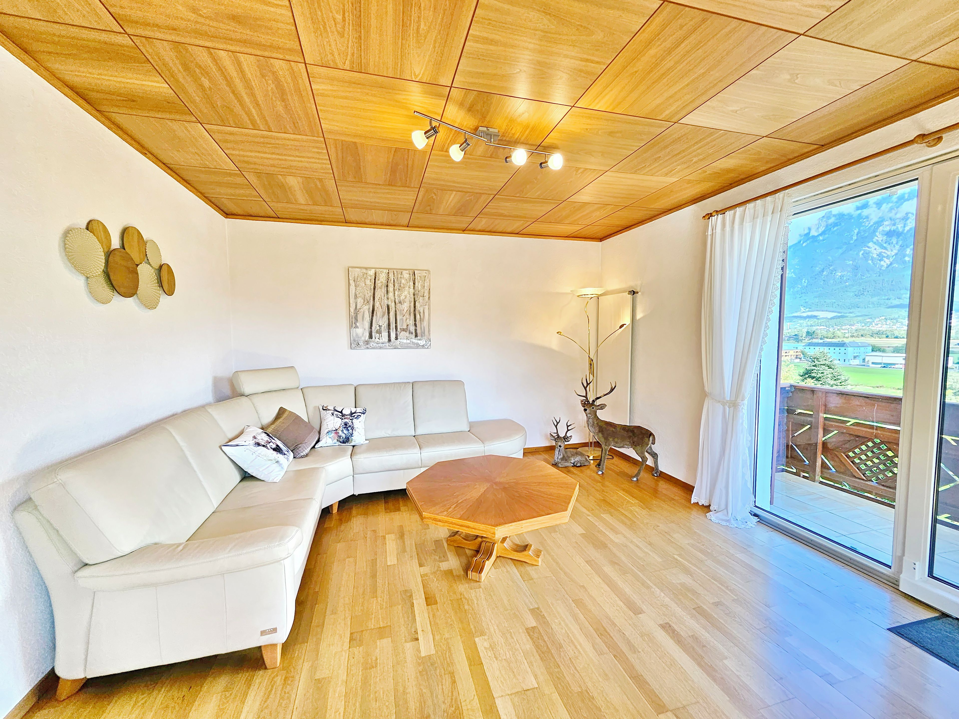 Ein modernes Wohnzimmer mit Holzbalkendecke, einem weißen Sofa, einem Holztisch und einer Hirschskulptur.