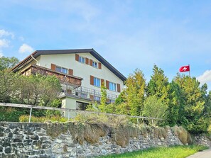 A two-story building with a balcony, surrounded by greenery and a stone wall. - Panorama House with a View of Three Countries (Sevelen)