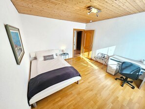 A bedroom with a bed, bedside table, lamp, desk, chair, and a door leading to another room. - Panorama House with a View of Three Countries (Sevelen)