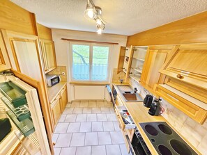 A compact kitchen with wooden cabinets, a built-in microwave, a stove, and a window with a view of greenery. - Panorama House with a View of Three Countries (Sevelen)