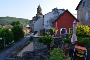 A courtyard with stone walls, a red building, and a church with a tower. - Vrbo Property (SAINT NECTAIRE)
