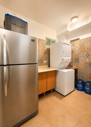 Une cuisine compacte équipée d’un réfrigérateur en acier inoxydable, d’un lave-linge blanc et d’un pare-feu en carrelage.