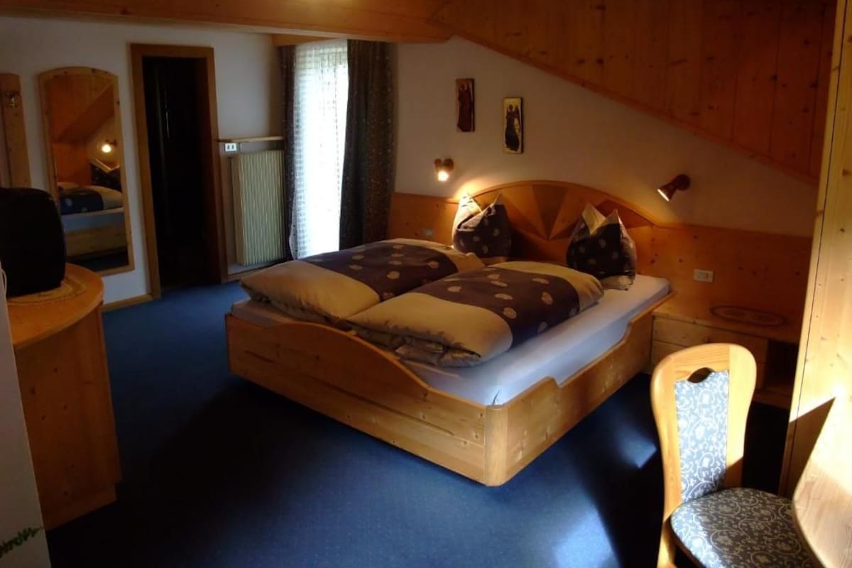 Quarto de madeira com uma cama, uma cadeira e uma mesa pequena.