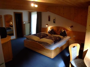 Quarto de madeira com uma cama, uma cadeira e uma mesa pequena.