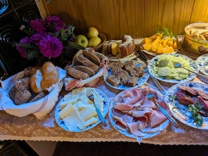 A table with various food items including bread, cheese, ham, and fruits. - Garni Conturina - B&B (Santa Cristina Valgardena)