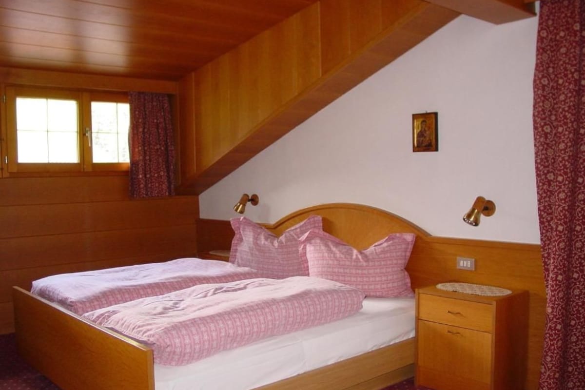 Quarto com cama de madeira, mesa de cabeceira, janela com cortinas e um pequeno quadro na parede.