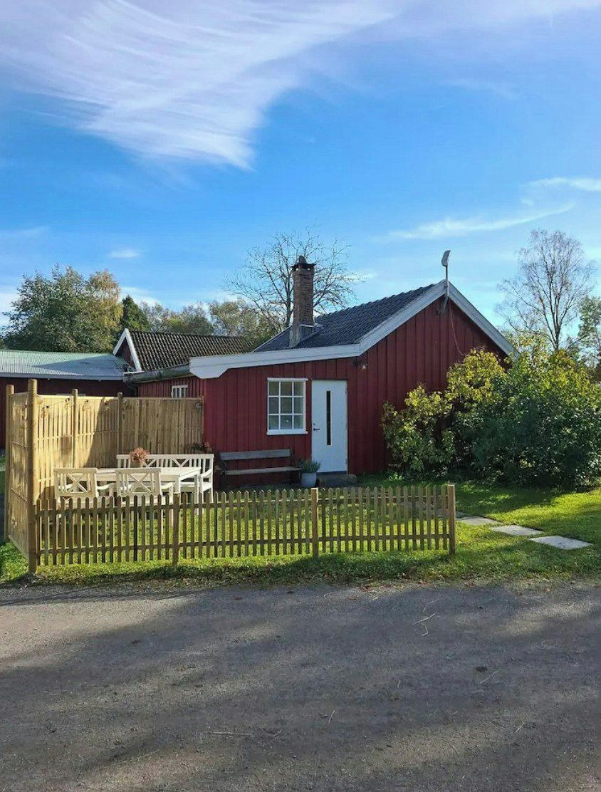 Un bâtiment rouge avec une porte blanche, un petit porche et une clôture en bois.