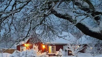 Un paysage enneigé avec une cabane en bois et un arbre au premier plan.