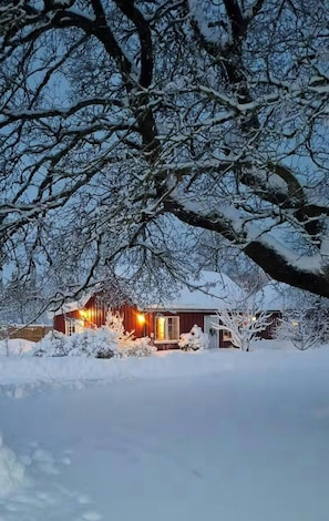 Paisaje nevado con una cabaña de madera y un árbol en primer plano.