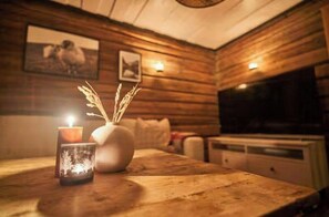 Un interior de madera con una mesa, una vela, un jarrón y una obra de arte en la pared.