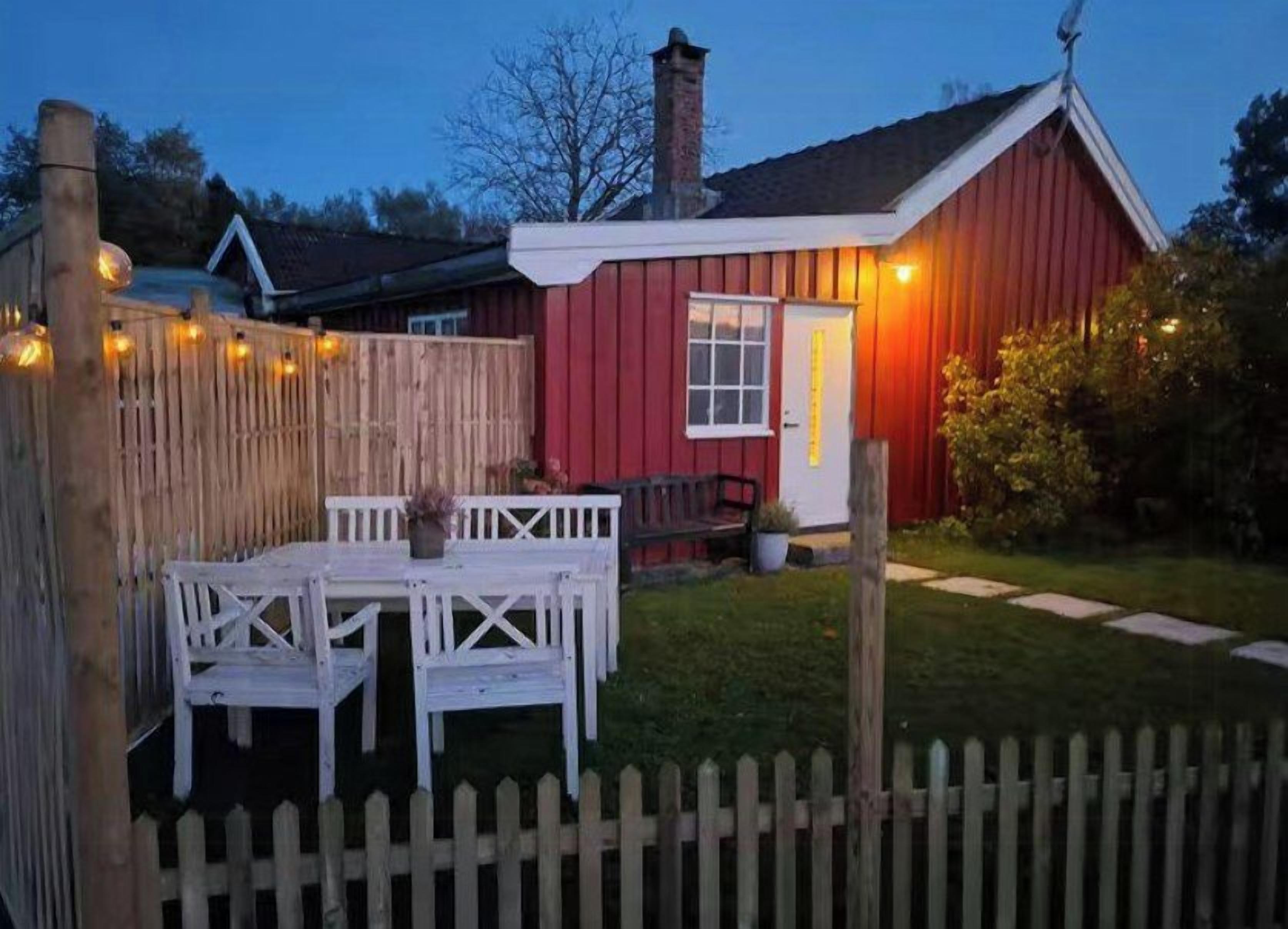 Un bâtiment rouge avec une porte blanche, une clôture en bois et une table blanche avec des chaises.
