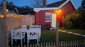 Un bâtiment rouge avec une porte blanche, une clôture en bois et une table blanche avec des chaises.