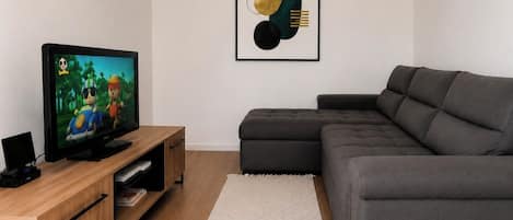 A modern living room with a flat-screen TV, a grey sectional sofa, a wooden entertainment unit, and a geometric abstract painting on the wall.