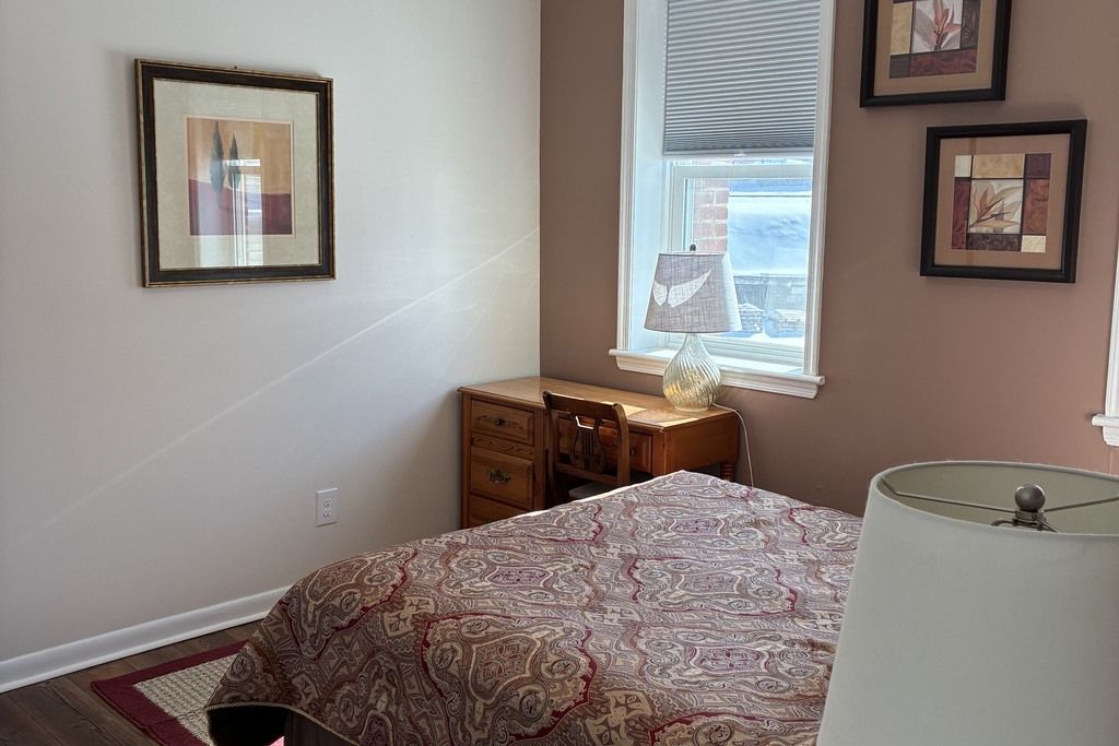 A bedroom with a bed, a dresser, a lamp, and framed artwork on the wall.