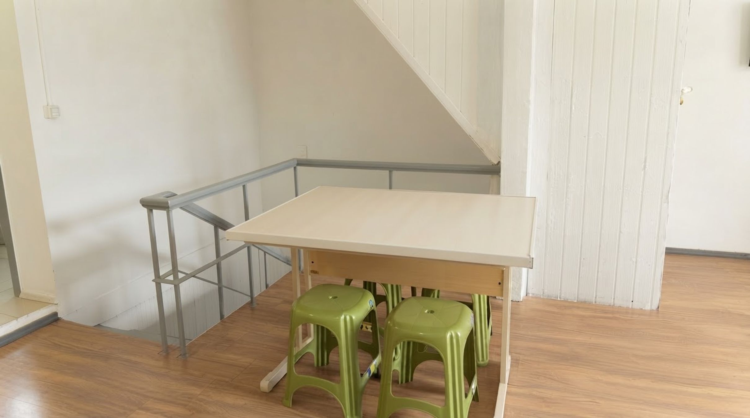 Ein Zimmer mit Holzboden, einem weißen Tisch und grünen Hocker.