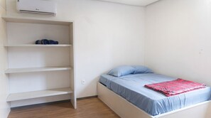 Quarto com cama, guarda-roupa branco e ar condicionado fixado na parede.