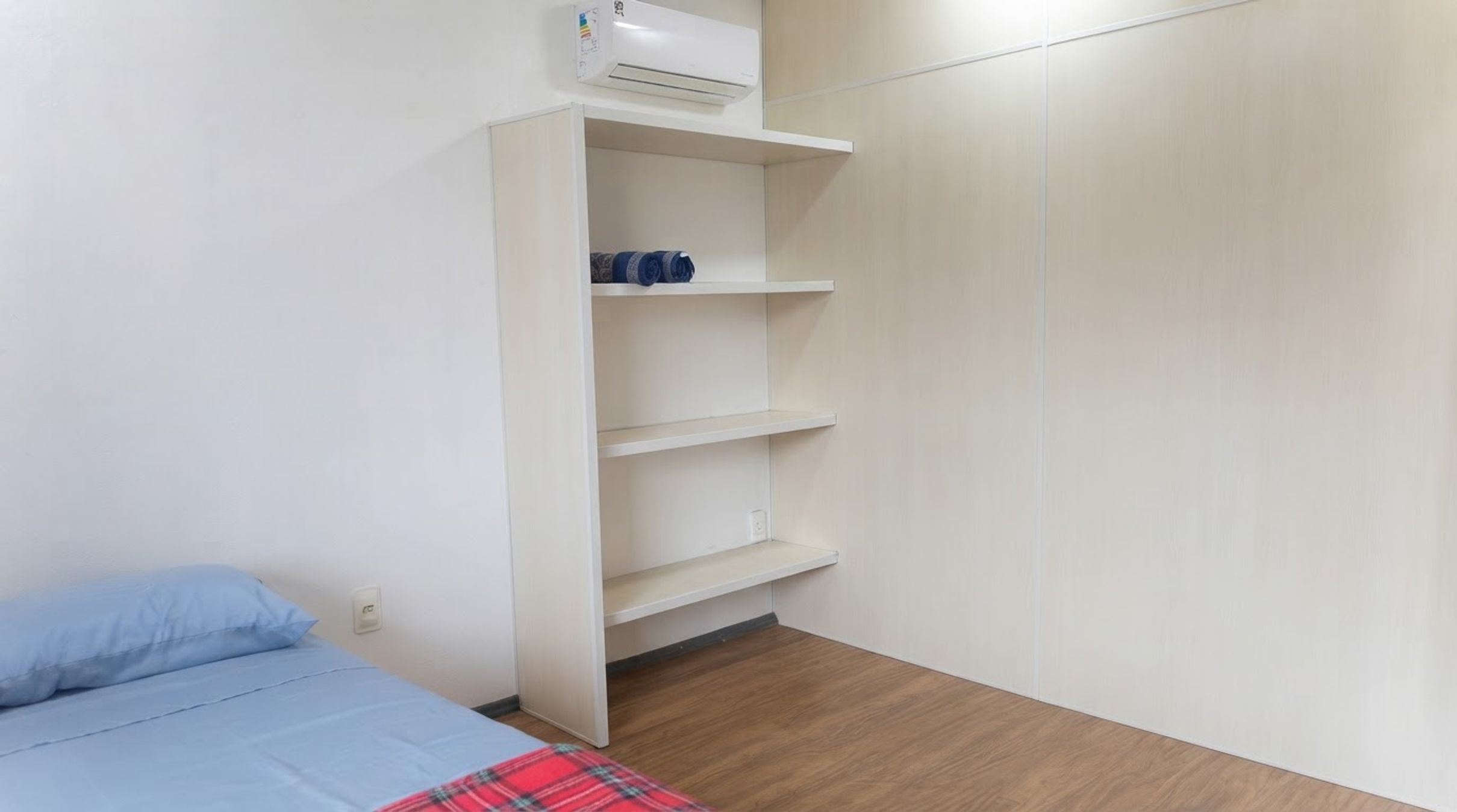 A bedroom with a bed, a wardrobe, and a wall-mounted air conditioner.