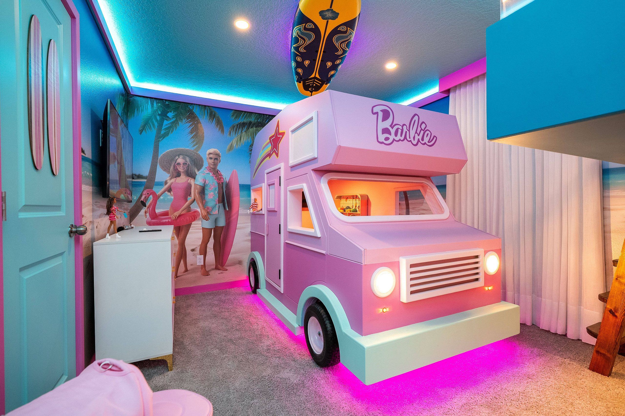 A room with a pink and white toy truck labeled 'Barbie' and a mural of two people on a beach.
