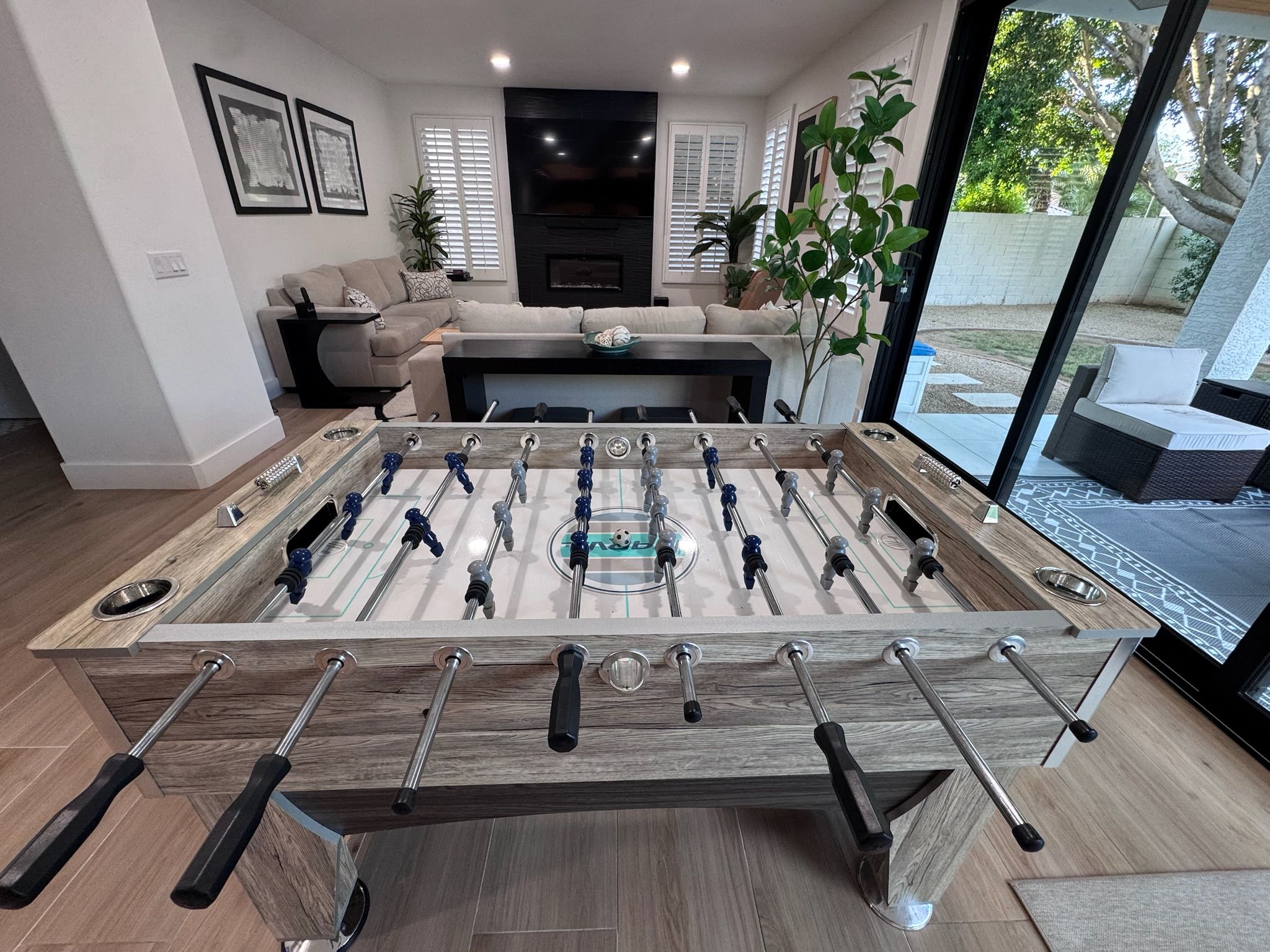 A modern living room with a foosball table, a sofa, and a large window offering a view of the outdoors.