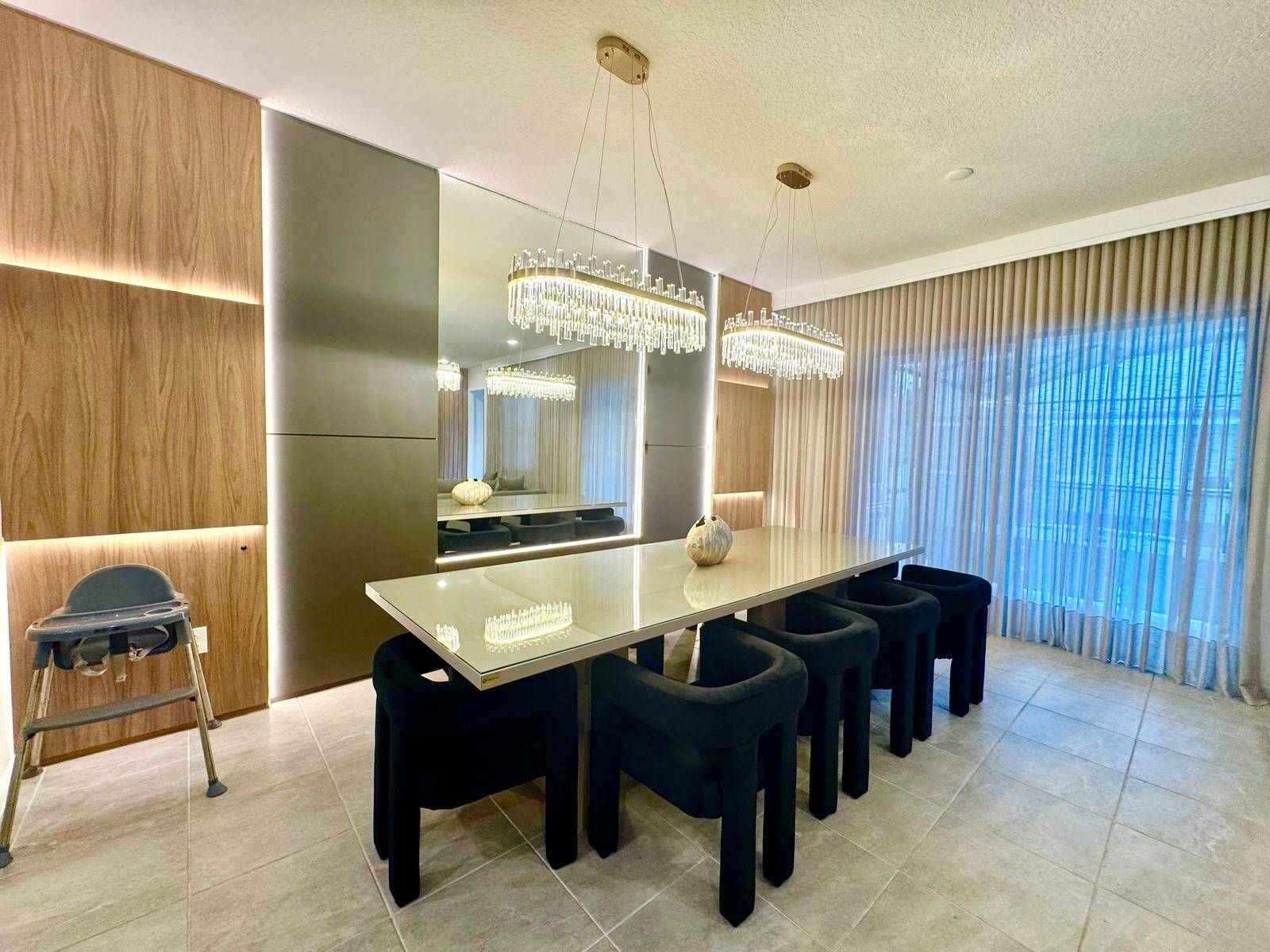 A modern dining area with a long table, multiple chairs, and a chandelier.