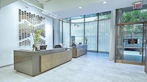 En moderne reception med glasdør, farvepalet på væggen og en disk med computer og plante.