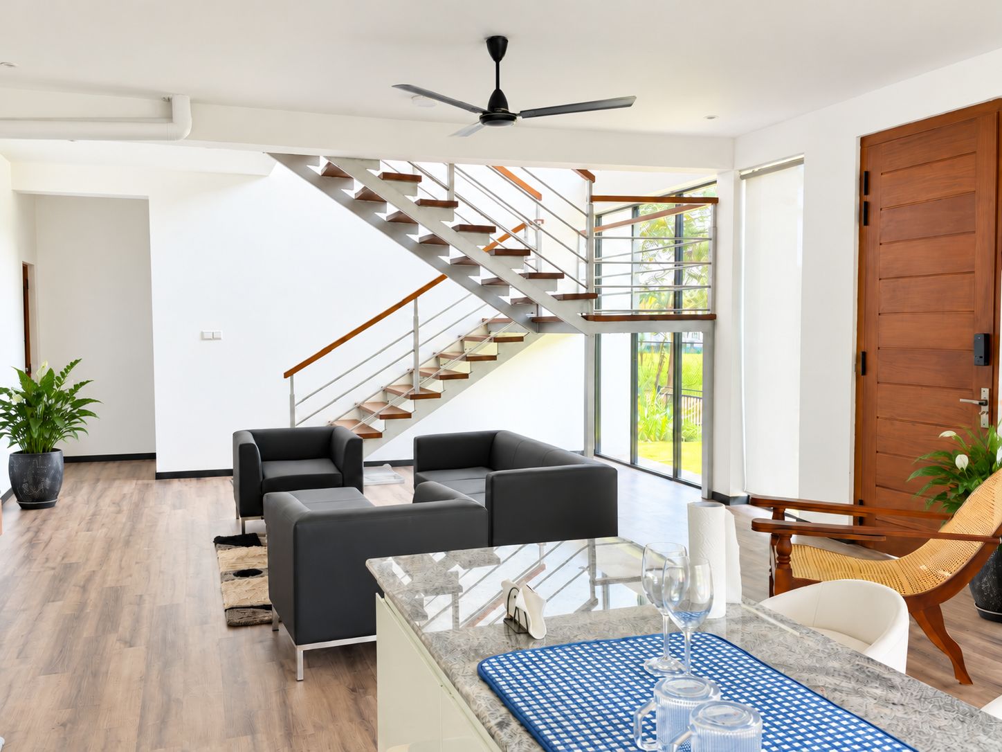 Ein modernes Wohnzimmer mit einem Glastisch, zwei Sofas, einem Esstisch mit Stühlen, einer Holztür und einer Wendeltreppe.