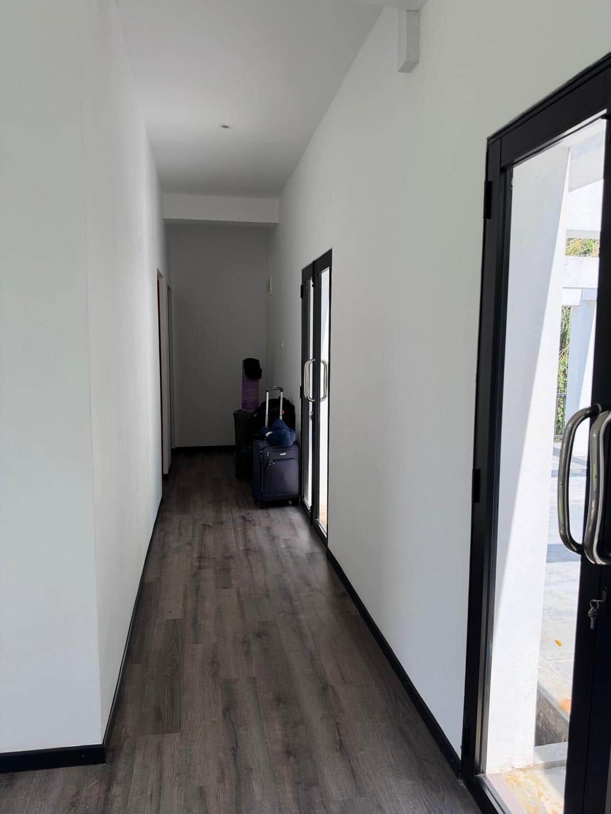 Un couloir avec un plancher en bois, une porte dotée d’une poignée et une fenêtre.