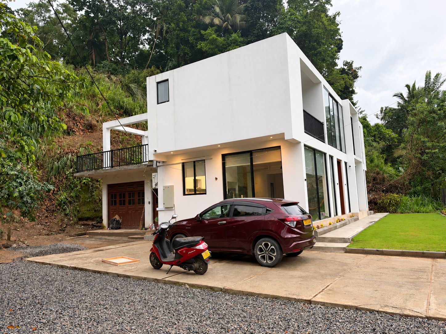 Une maison moderne à deux étages, avec une voiture garée dans l’allée et un scooter sur le porche.