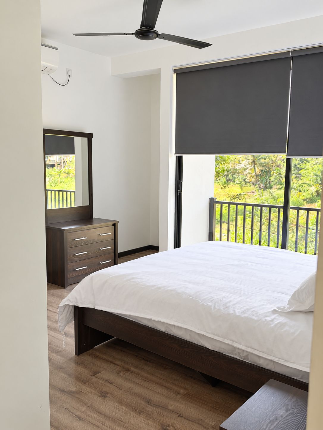 Un dormitorio con cama, cómoda, ventilador de techo y ventana con vistas a la vegetación.