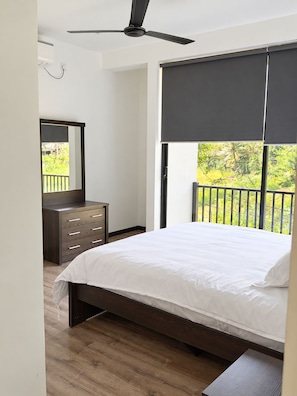 Une chambre à coucher comprenant un lit, une commode, un ventilateur de plafond et une fenêtre donnant sur un paysage verdoyant.