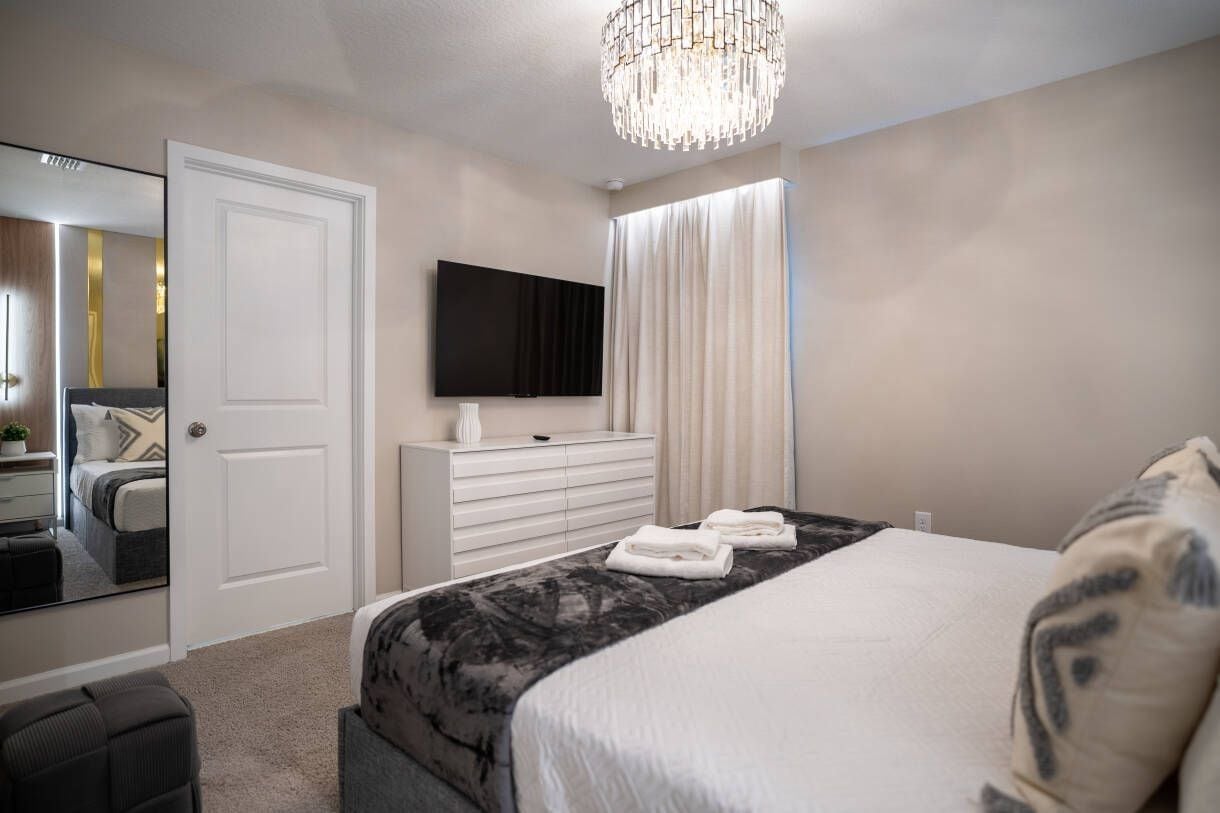 A bedroom with a bed, a TV, a dresser, and a mirror.