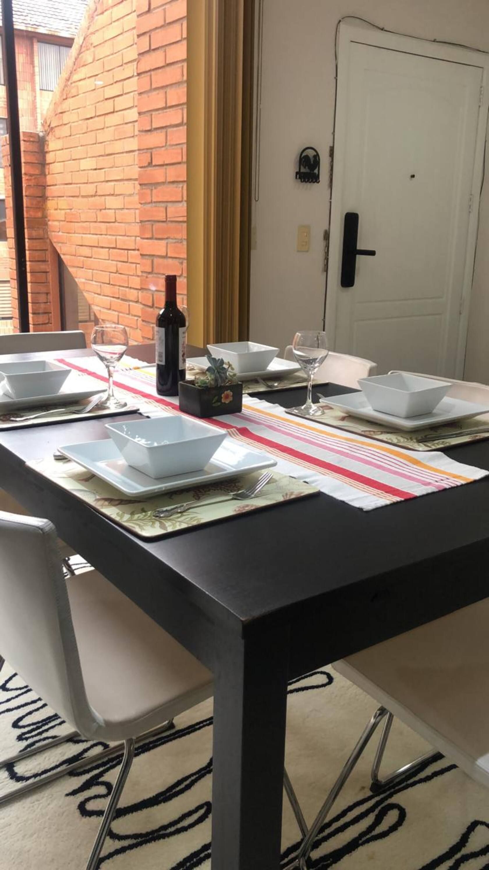 A dining table set with white plates, bowls, and cutlery, a bottle of wine, and a striped placemat.